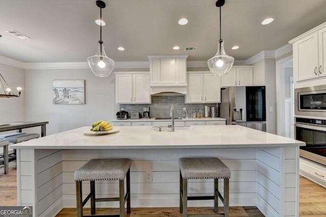 kitchen featuring hanging light fixtures, stainless steel appliances, an island with sink, and white cabinets