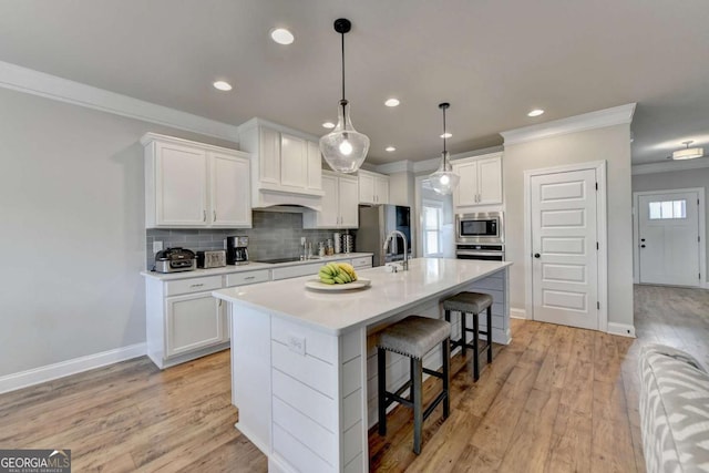 kitchen featuring stainless steel appliances, an island with sink, white cabinets, and a kitchen bar