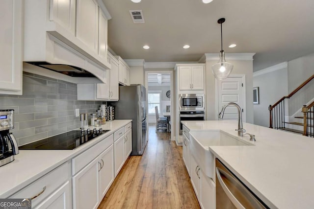 kitchen with sink, white cabinetry, hanging light fixtures, appliances with stainless steel finishes, and light hardwood / wood-style floors