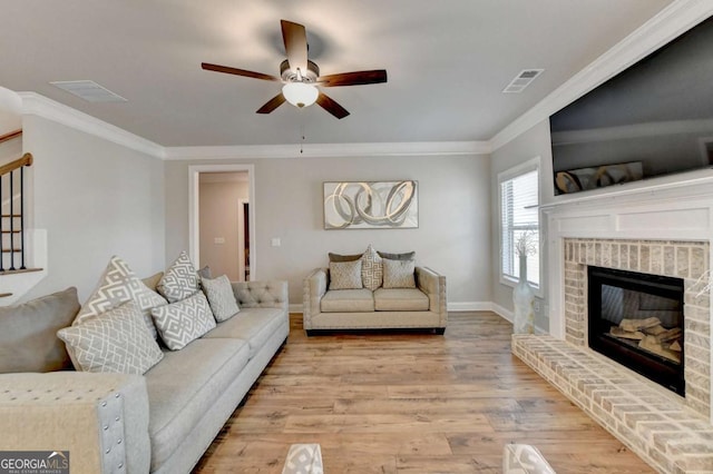 living room featuring a brick fireplace, light hardwood / wood-style flooring, ornamental molding, and ceiling fan