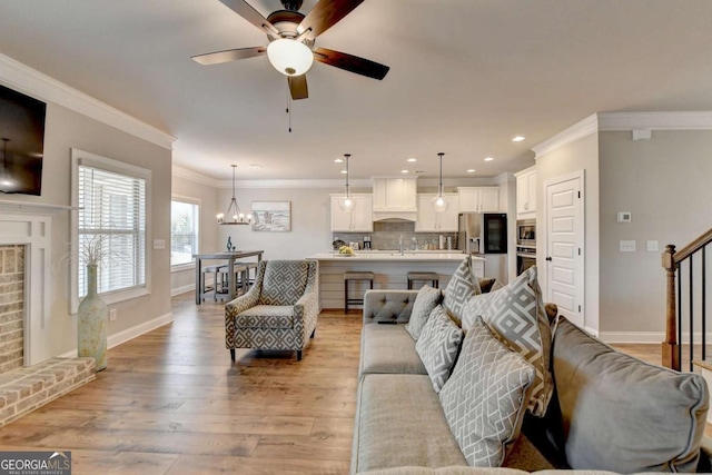 living room featuring sink, crown molding, light hardwood / wood-style flooring, a fireplace, and ceiling fan with notable chandelier