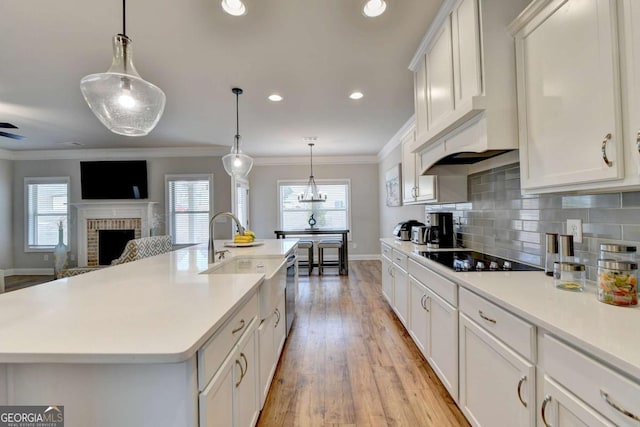 kitchen with an island with sink, black electric stovetop, white cabinets, and decorative light fixtures