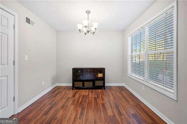 spare room featuring an inviting chandelier and dark wood-type flooring