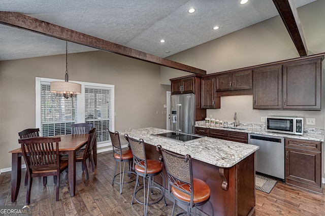 kitchen with appliances with stainless steel finishes, a sink, lofted ceiling with beams, and a kitchen island