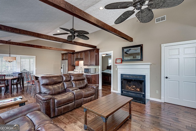 living area with a textured ceiling, vaulted ceiling with beams, visible vents, a lit fireplace, and dark wood finished floors