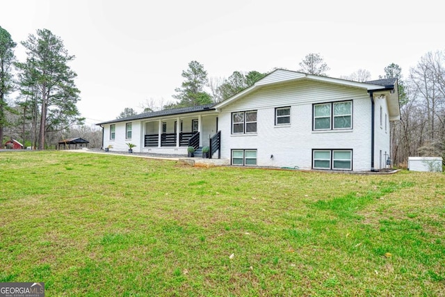 rear view of house featuring covered porch, brick siding, and a yard