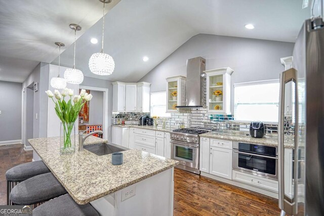 kitchen with stainless steel appliances, a breakfast bar, dark wood-type flooring, a sink, and wall chimney exhaust hood