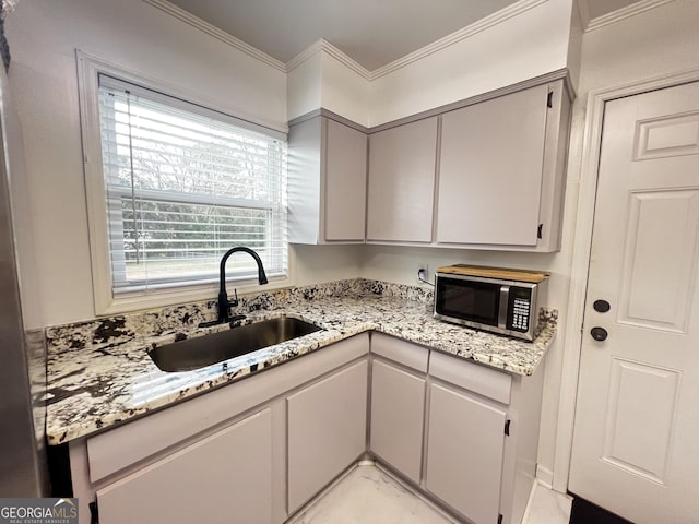 kitchen with light stone counters, stainless steel microwave, ornamental molding, and a sink