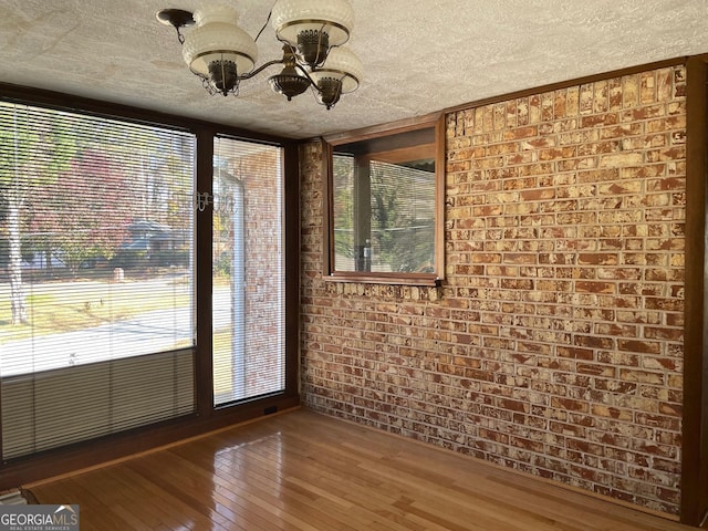 spare room with hardwood / wood-style flooring, brick wall, and a textured ceiling