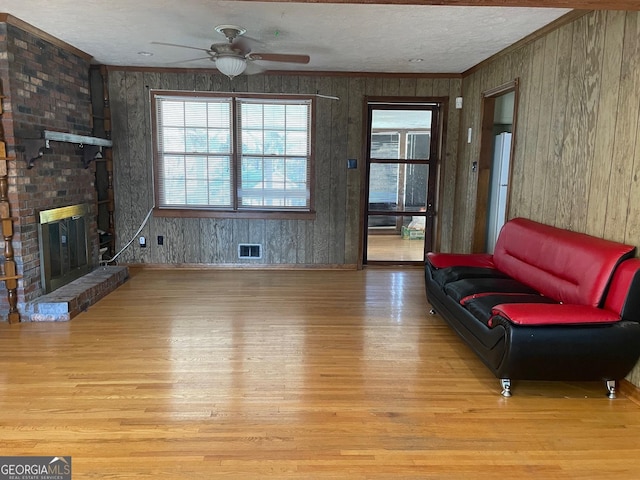 living room featuring crown molding, ceiling fan, light hardwood / wood-style floors, a textured ceiling, and a brick fireplace