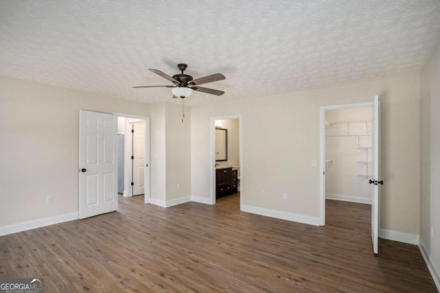 unfurnished bedroom with ensuite bathroom, dark hardwood / wood-style floors, a textured ceiling, and a spacious closet