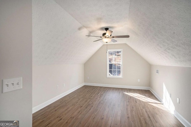 additional living space with vaulted ceiling, hardwood / wood-style floors, ceiling fan, and a textured ceiling