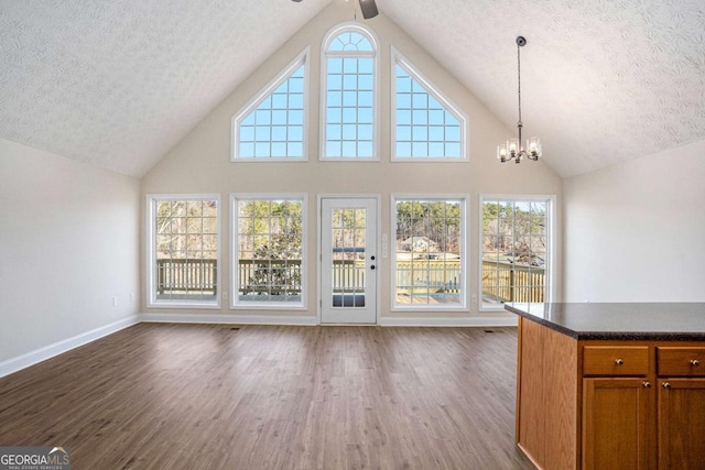 unfurnished living room with dark wood-type flooring, lofted ceiling, ceiling fan with notable chandelier, and a textured ceiling