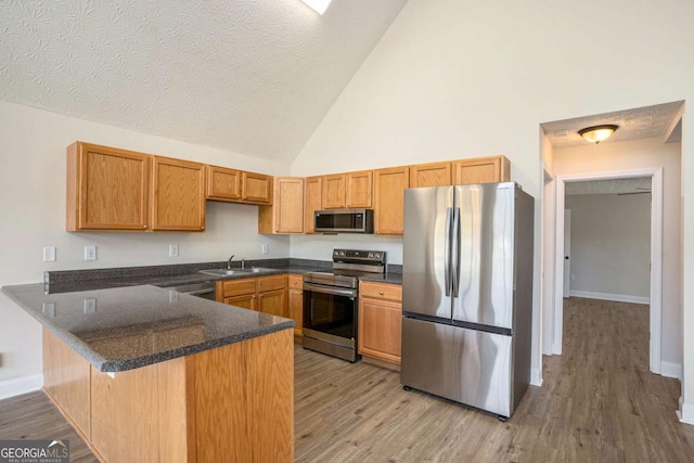 kitchen with appliances with stainless steel finishes, sink, light hardwood / wood-style floors, kitchen peninsula, and a textured ceiling