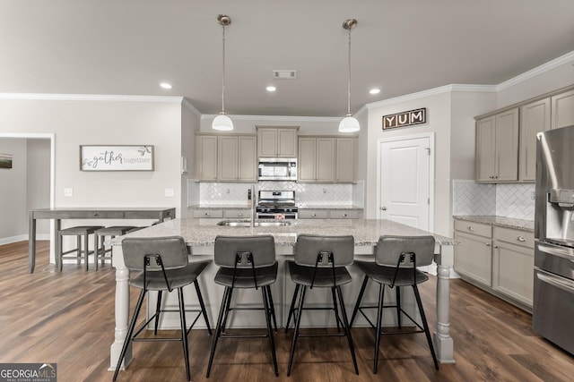 kitchen featuring light stone counters, decorative light fixtures, a center island with sink, and appliances with stainless steel finishes