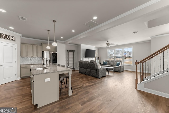 kitchen with sink, a breakfast bar area, light stone counters, a center island with sink, and stainless steel refrigerator