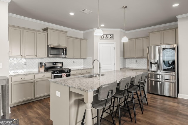 kitchen with sink, light stone counters, an island with sink, pendant lighting, and stainless steel appliances