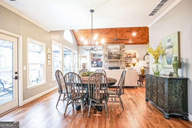 dining area featuring a stone fireplace, crown molding, vaulted ceiling, light hardwood / wood-style flooring, and a notable chandelier