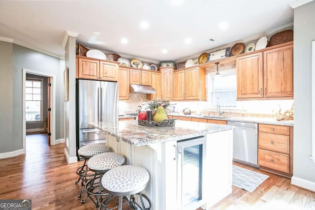 kitchen with stainless steel appliances, a center island, beverage cooler, and light stone counters