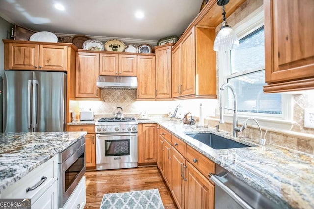 kitchen with sink, stainless steel appliances, hanging light fixtures, and light stone countertops