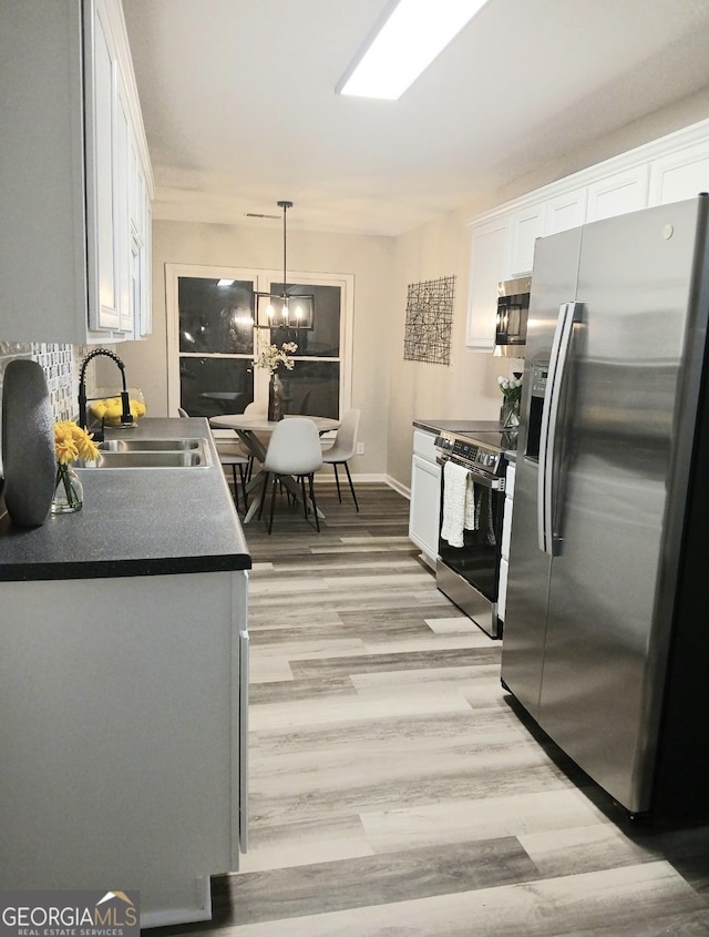 kitchen with appliances with stainless steel finishes, sink, white cabinets, and decorative light fixtures