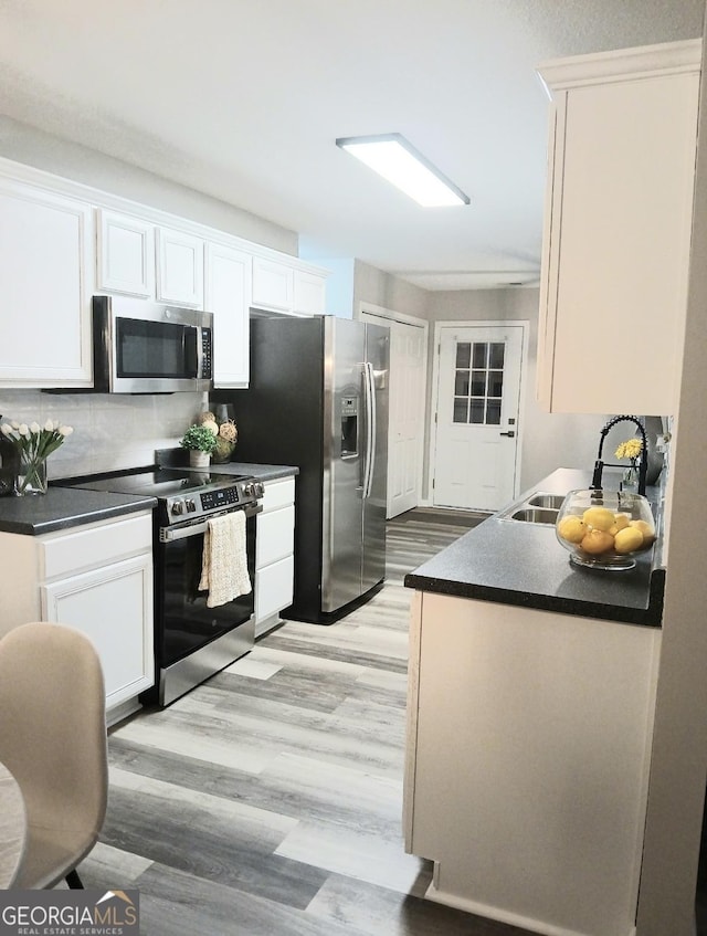 kitchen with appliances with stainless steel finishes, sink, light hardwood / wood-style flooring, and white cabinets