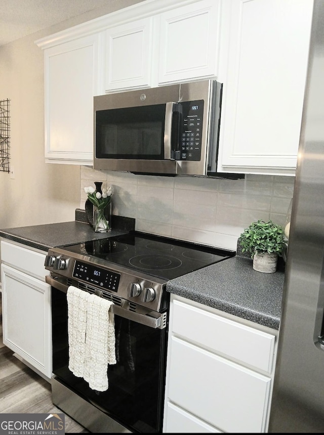 kitchen with backsplash, light wood-type flooring, white cabinets, and appliances with stainless steel finishes