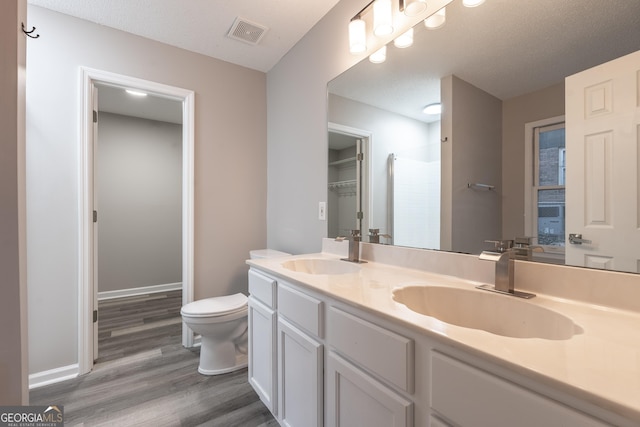 bathroom with walk in shower, vanity, toilet, and wood-type flooring