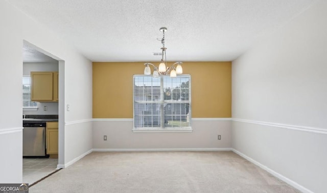 carpeted empty room featuring plenty of natural light, a textured ceiling, and an inviting chandelier