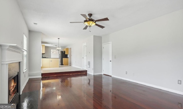 unfurnished living room featuring ceiling fan with notable chandelier and dark hardwood / wood-style floors