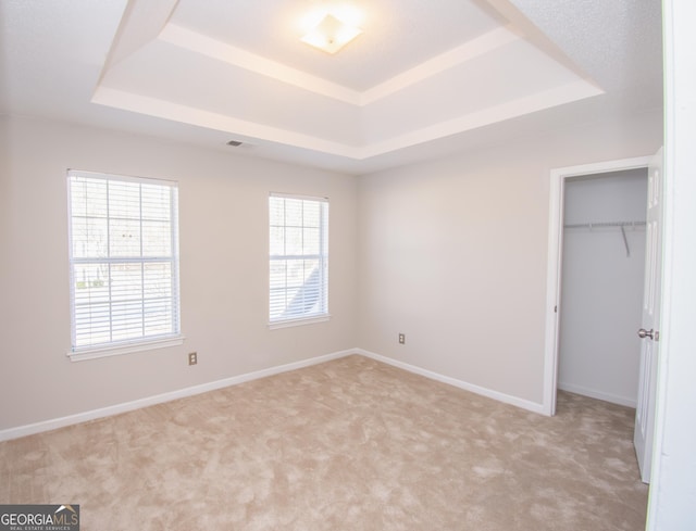 unfurnished bedroom featuring light colored carpet, a raised ceiling, and multiple windows