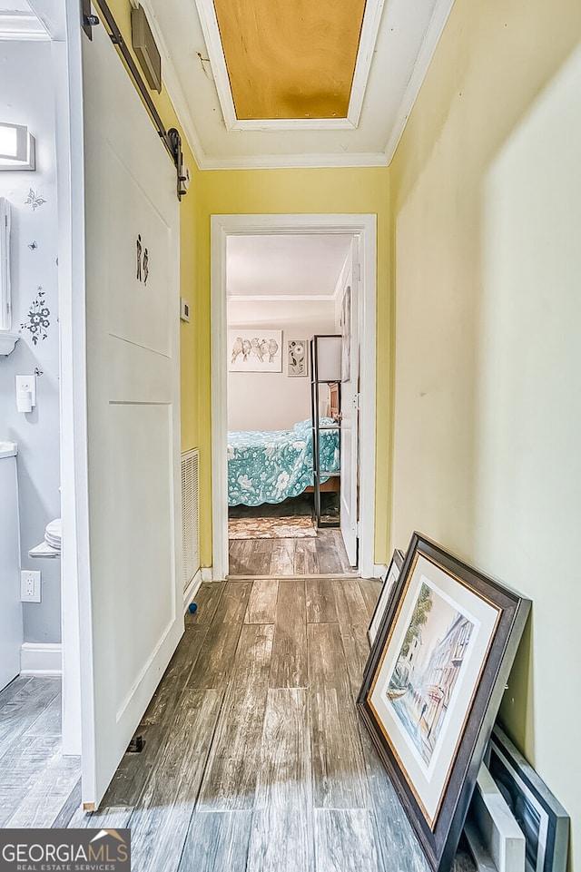 corridor featuring a barn door, baseboards, visible vents, ornamental molding, and wood finished floors