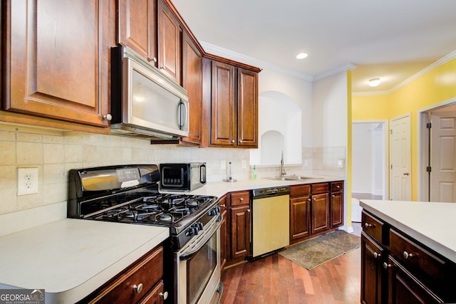 kitchen with ornamental molding, a sink, dark wood-style floors, appliances with stainless steel finishes, and light countertops