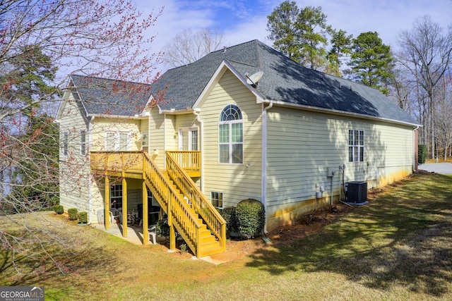 back of property featuring a deck, a yard, cooling unit, a shingled roof, and stairs