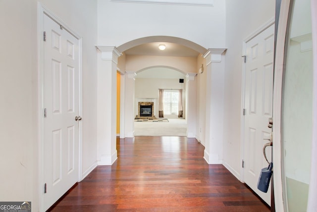 hallway featuring arched walkways, baseboards, ornate columns, and wood finished floors