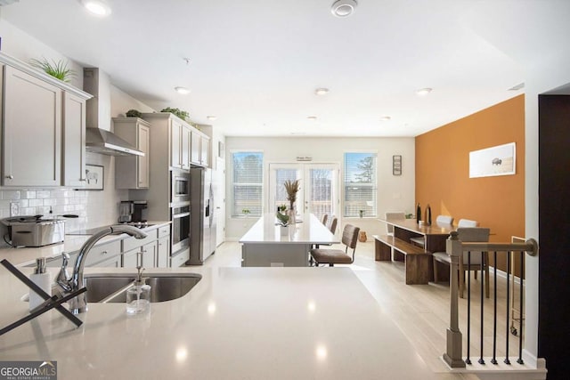 kitchen featuring wall chimney range hood, sink, appliances with stainless steel finishes, gray cabinetry, and backsplash