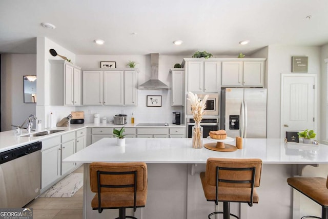 kitchen with wall chimney range hood, sink, a breakfast bar area, stainless steel appliances, and decorative backsplash