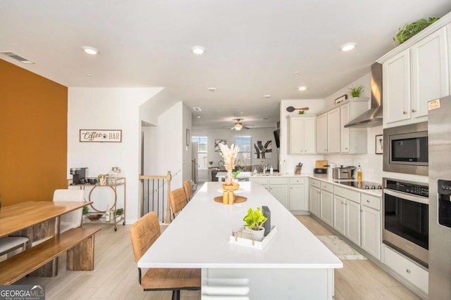 kitchen with sink, a kitchen breakfast bar, stainless steel appliances, a center island, and wall chimney exhaust hood