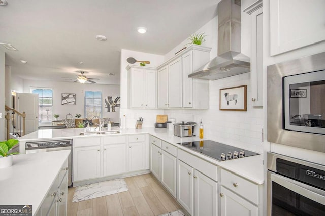 kitchen with appliances with stainless steel finishes, white cabinetry, sink, kitchen peninsula, and wall chimney exhaust hood