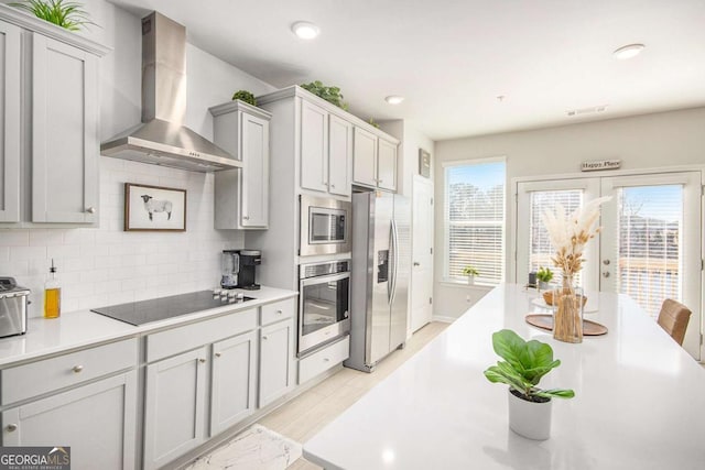 kitchen with wall chimney exhaust hood, tasteful backsplash, light hardwood / wood-style flooring, gray cabinets, and stainless steel appliances