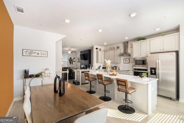 kitchen featuring a breakfast bar, white cabinetry, a kitchen island with sink, stainless steel appliances, and wall chimney exhaust hood