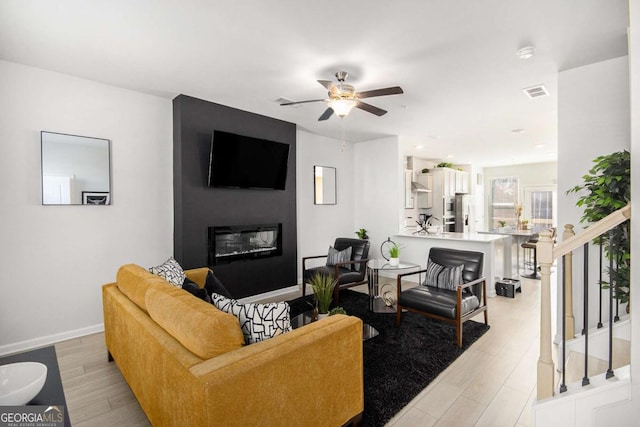 living room with ceiling fan, a large fireplace, and light hardwood / wood-style flooring