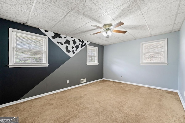 empty room featuring ceiling fan, plenty of natural light, carpet flooring, and a drop ceiling