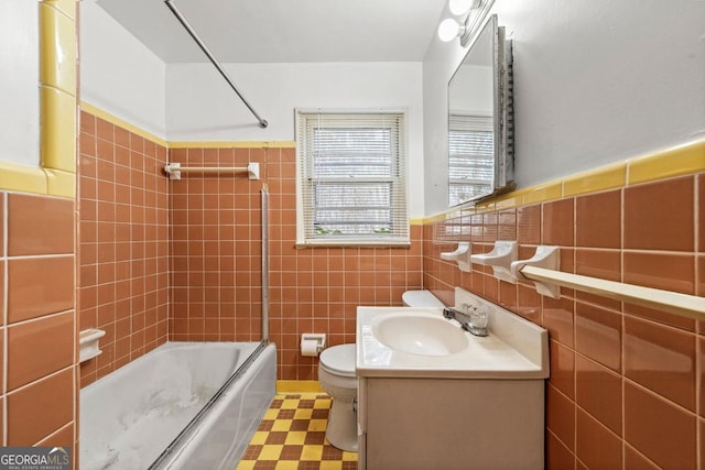 full bathroom featuring toilet, vanity, shower / bath combination with glass door, and tile walls