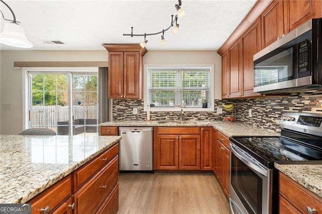 kitchen with sink, decorative light fixtures, light hardwood / wood-style flooring, stainless steel appliances, and light stone countertops