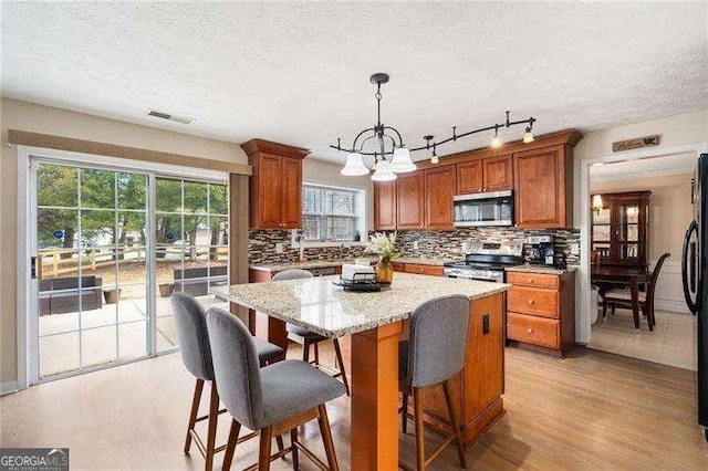 kitchen with pendant lighting, light hardwood / wood-style flooring, stainless steel appliances, light stone countertops, and a kitchen island