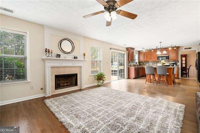 living room featuring ceiling fan, plenty of natural light, dark wood-type flooring, and a textured ceiling