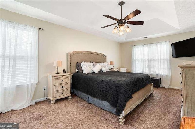 carpeted bedroom featuring ceiling fan and a tray ceiling