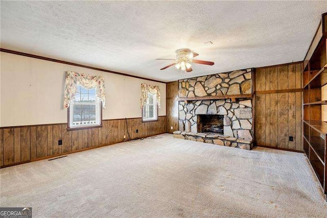 unfurnished living room featuring ceiling fan, a fireplace, a textured ceiling, and wood walls