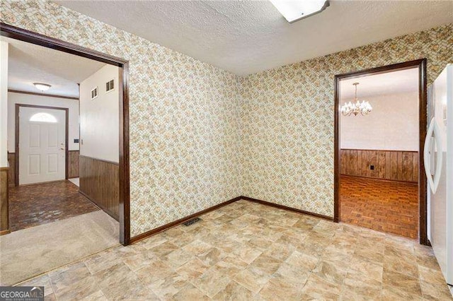 empty room featuring an inviting chandelier, a textured ceiling, and wood walls